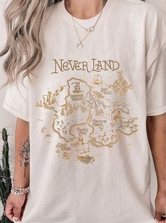 a woman wearing a white t - shirt that says never land with gold foil on it