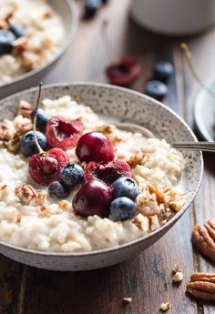 two bowls filled with oatmeal topped with berries and pecans next to nuts