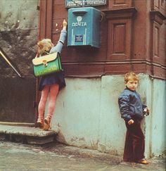 two young children standing next to each other in front of a building with a mailbox on the wall