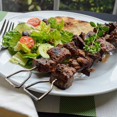 a white plate topped with meat and salad next to a fork on top of a table