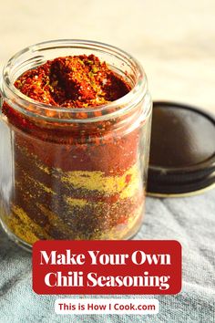 a jar filled with chili seasoning sitting on top of a blue cloth next to a spoon