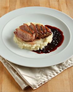 a white plate topped with meat and mashed potatoes covered in sauce on top of a wooden table