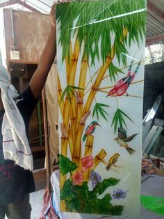 a woman holding up a painting with birds and bamboo trees on it in front of a building