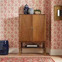 a wooden cabinet sitting in the corner of a room next to a rug and wall paper