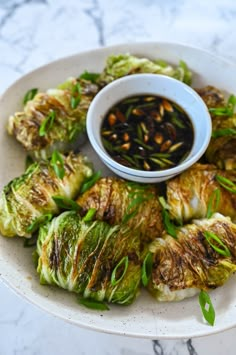 a white plate topped with brussel sprouts next to a bowl of dipping sauce