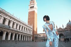 a woman standing in front of a tall building with a clock tower on it's side