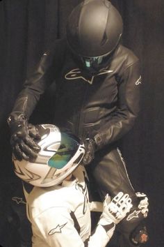 a man in black and white motorcycle gear is holding the helmet of another person's hand