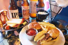 a plate topped with a sandwich and french fries next to bottles of beer on a table