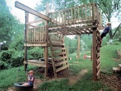 a child on a swing set in the grass near a wooden structure with stairs and ladders