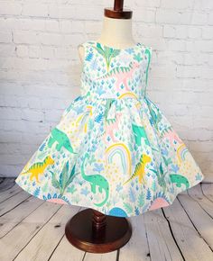 Display dress is a size 3t on a size 3t mannequin. It is shown with tulle petticoat which is NOT INCLUDED in the purchase of this dress. It is for display purposes only. This little pastel dinosaur dress features multi colored dinosaurs in a tropical jungle setting on a cream colored background . It would be perfect for a dinosaur themed birthday party or for any little one that loves dinos! The bodice is lined with soft cotton and it snaps in the back with Kam snaps for easy on and off. There a Summer Fitted Princess Dress, Cute A-line Dress For Dress-up Occasions, Fitted Princess Summer Dresses, Cute Green A-line Dress, Playful Fitted Ruffled Princess Dress, Playful Fitted Princess Dress With Ruffles, Playful Fitted Dress For Dress-up Occasions, Playful Fitted Dresses For Dress-up, Fitted Princess Sleeveless Dress With Ruffles