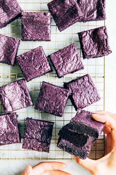 purple cake squares on a cooling rack being held by someone's hands with their fingers