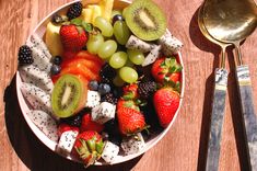 a white bowl filled with fruit next to a fork and spoon on top of a wooden table