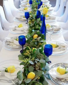 a long table is set with blue glassware and yellow flowers