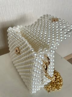 a white beaded purse with gold chains and pearls on the front, sitting on a table