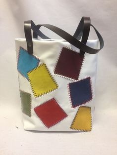 a white bag with different colored squares on the front and sides, hanging from a black leather strap