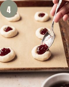 someone spooning jam onto small cookies on a baking sheet