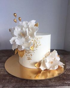 a white and gold wedding cake with flowers on the top is sitting on a wooden table