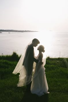 a bride and groom standing in front of the water at sunset on their wedding day