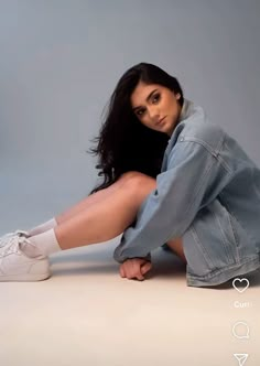 a woman is sitting on the floor with her legs crossed wearing white tennis shoes and denim jacket