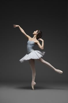 a young ballerina in white and grey is posing with her arms out to the side