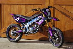 a purple and black dirt bike parked in front of a wooden garage door with the number 70 on it