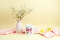 a pink vase with flowers in it next to a white mug and some lemons