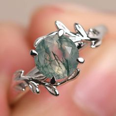 a close up of a person holding a ring with a green stone in the middle