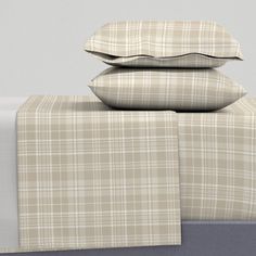 three pillows are stacked on top of each other in front of a bed with plaid sheets