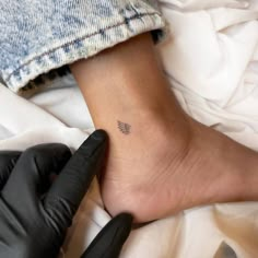 a person with a black glove on their foot and a small wing tattoo on the ankle