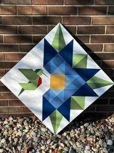 a colorful quilt sitting on top of a pile of rocks next to a brick wall