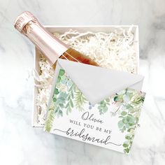 a bottle of champagne sitting in a box next to a card with the words, queen will you be my bridesmaid