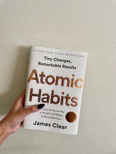 a person holding up a book with the title atomic habitts written in brown ink