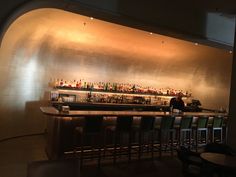 a bar with lots of bottles on the wall and chairs at the counter in front of it