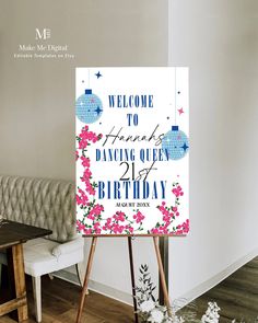 a welcome sign with flowers on it in front of a white couch and wooden easel