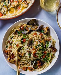 pasta with clams and vegetables in a bowl next to a glass of wine