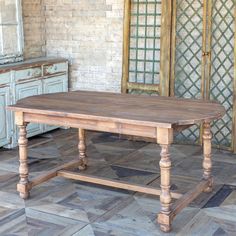 an old wooden table sitting on top of a tile floor next to a brick wall