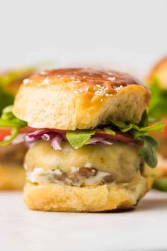 a hamburger with lettuce, tomato and cheese on it sitting on a white surface