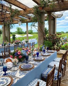 an outdoor dining area with blue and white table cloths, place settings and floral centerpieces