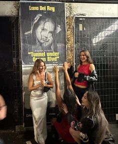 some girls are standing in front of a poster and one girl is holding her hand up