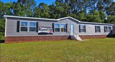 a mobile home for sale in the middle of a grassy area with trees behind it