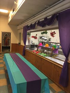 a table with purple and blue cloth on it in front of a window filled with decorations