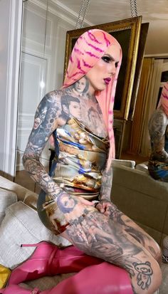 a woman with pink hair and tattoos sitting on a couch in front of a mirror