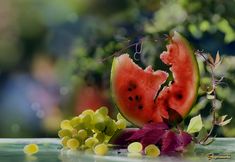 two slices of watermelon and grapes on a table with green leaves around them