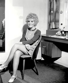 a black and white photo of a woman sitting on a chair in front of a mirror