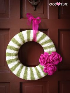 a knitted wreath with pink flowers hanging on the front door, next to a brown door