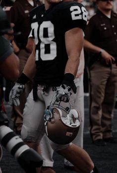 a football player is holding his helmet and walking on the field with other players in the background