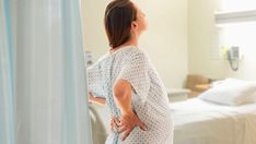 a woman in a hospital gown is looking up at the ceiling while standing next to a bed