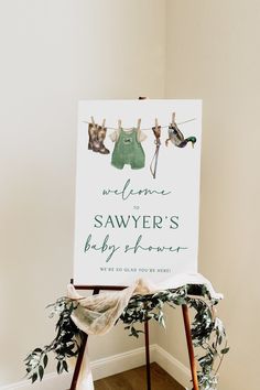 a baby shower sign with clothes hanging on the clothesline next to it's wooden easel