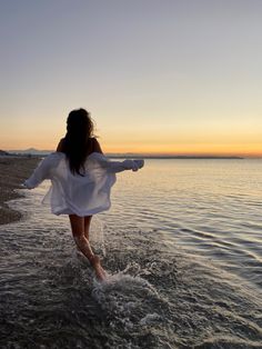 a woman walking into the ocean at sunset