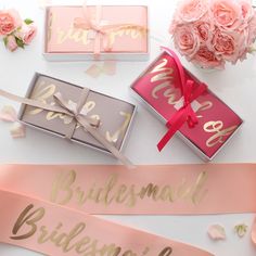 bridesmaid sashes and pink roses on a white table with gold foil lettering